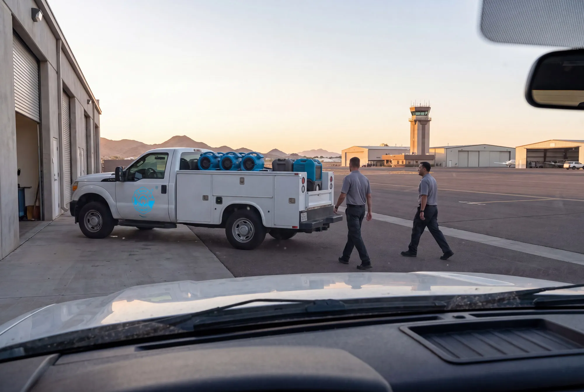 A Water Fighters truck pulls out of a north Phoenix industrial bay at dawn with the Deer Valley airport corridor behind it.