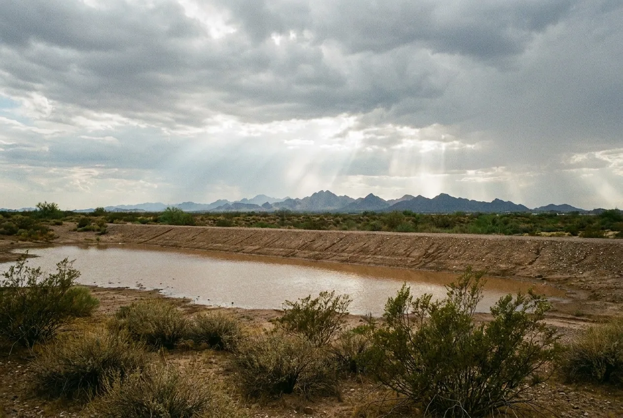 A shallow pool of storm runoff collects against a long earthen flood-control dam north of Interstate 10 near Buckeye.