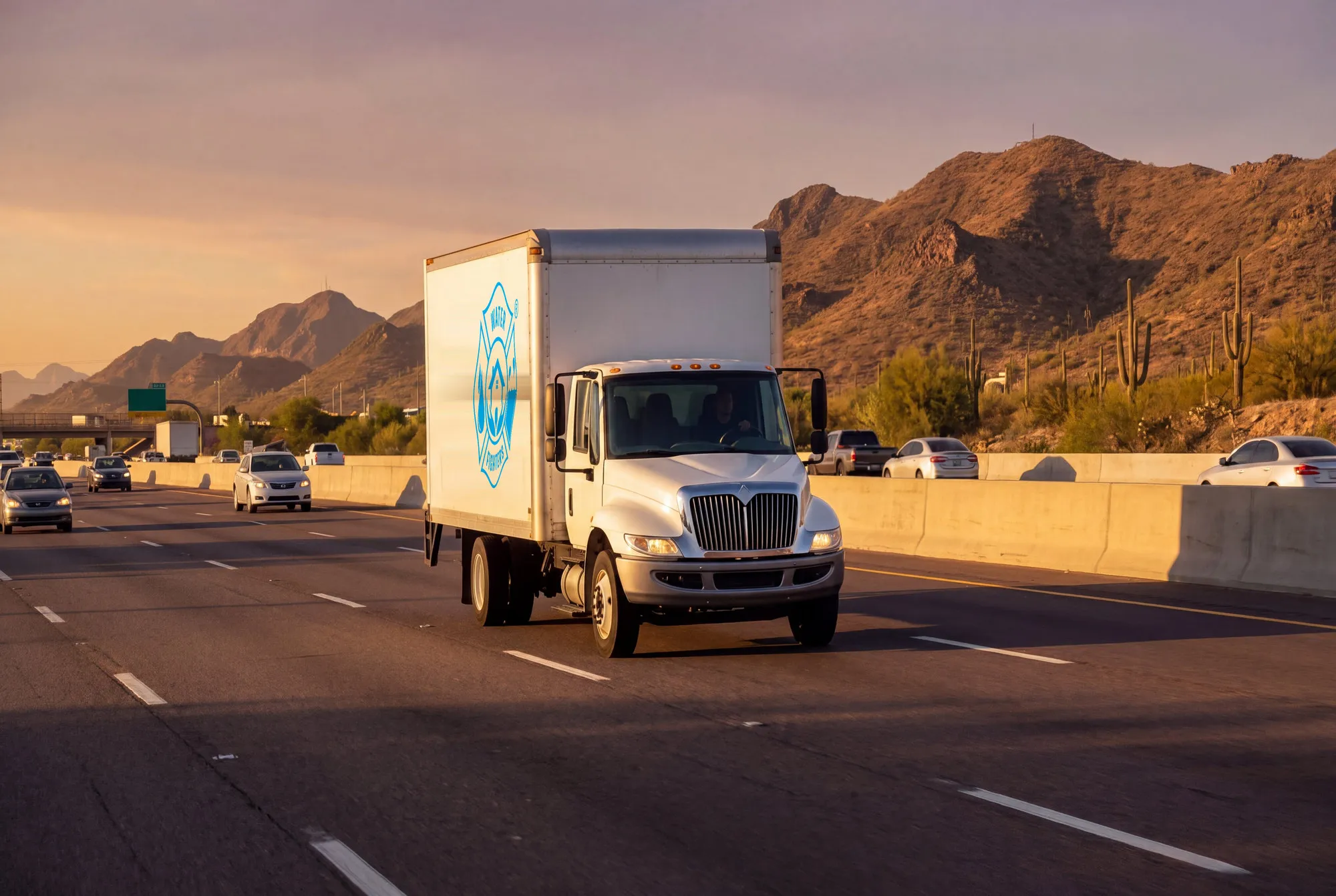 A Water Fighters service truck on a Phoenix Valley freeway at sunrise with desert mountains in the background.